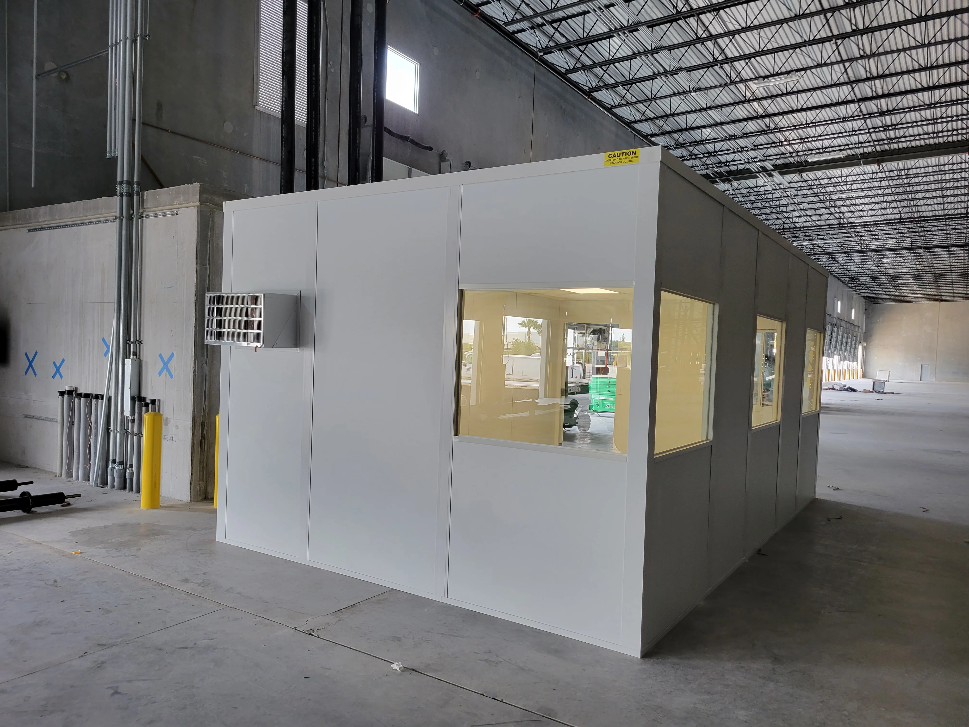 White drywall modular office with yellow-framed glass openings and HVAC unit in warehouse