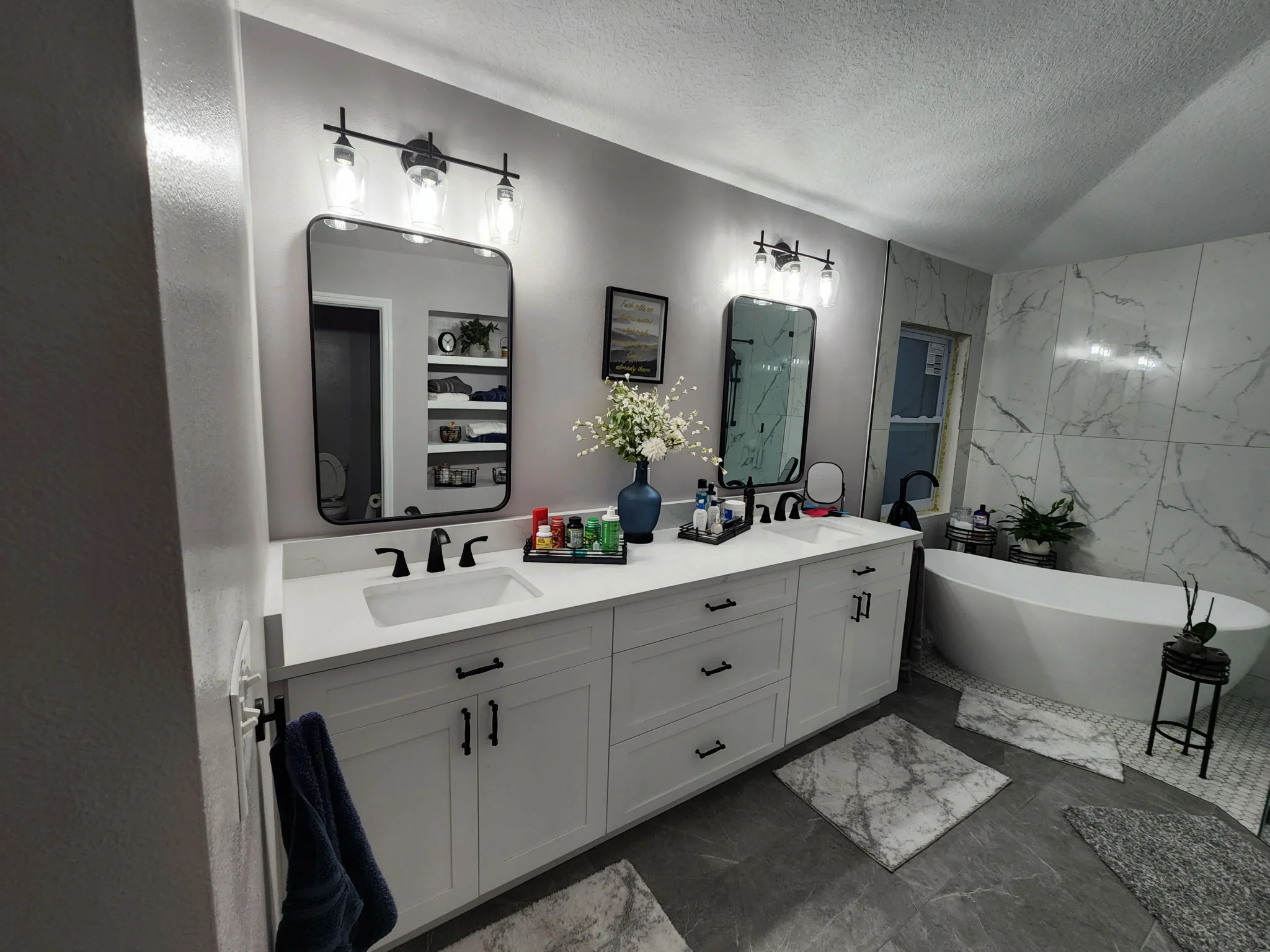 White vanity with quartz countertop, dual mirrors, marble tile walls, and freestanding tub in renovated bathroom