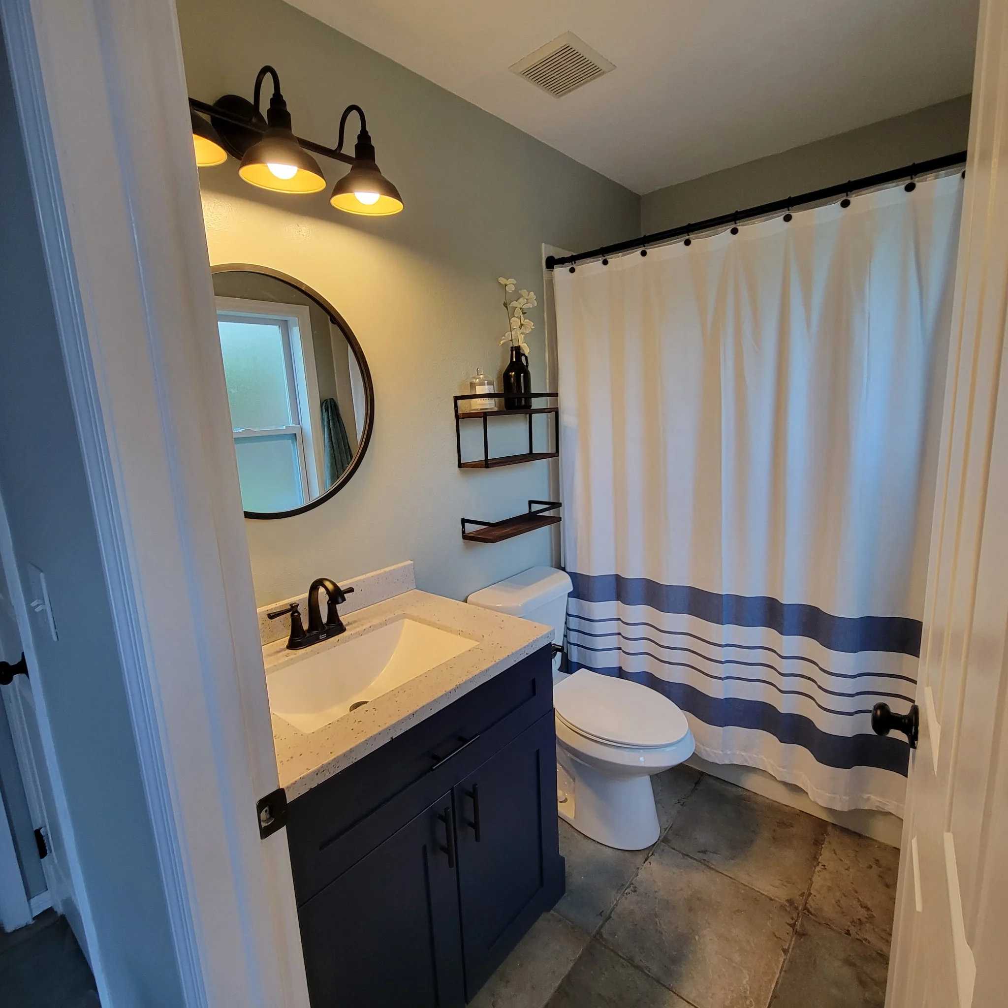 Bathroom with navy vanity, quartz countertop, black fixtures, and striped shower curtain