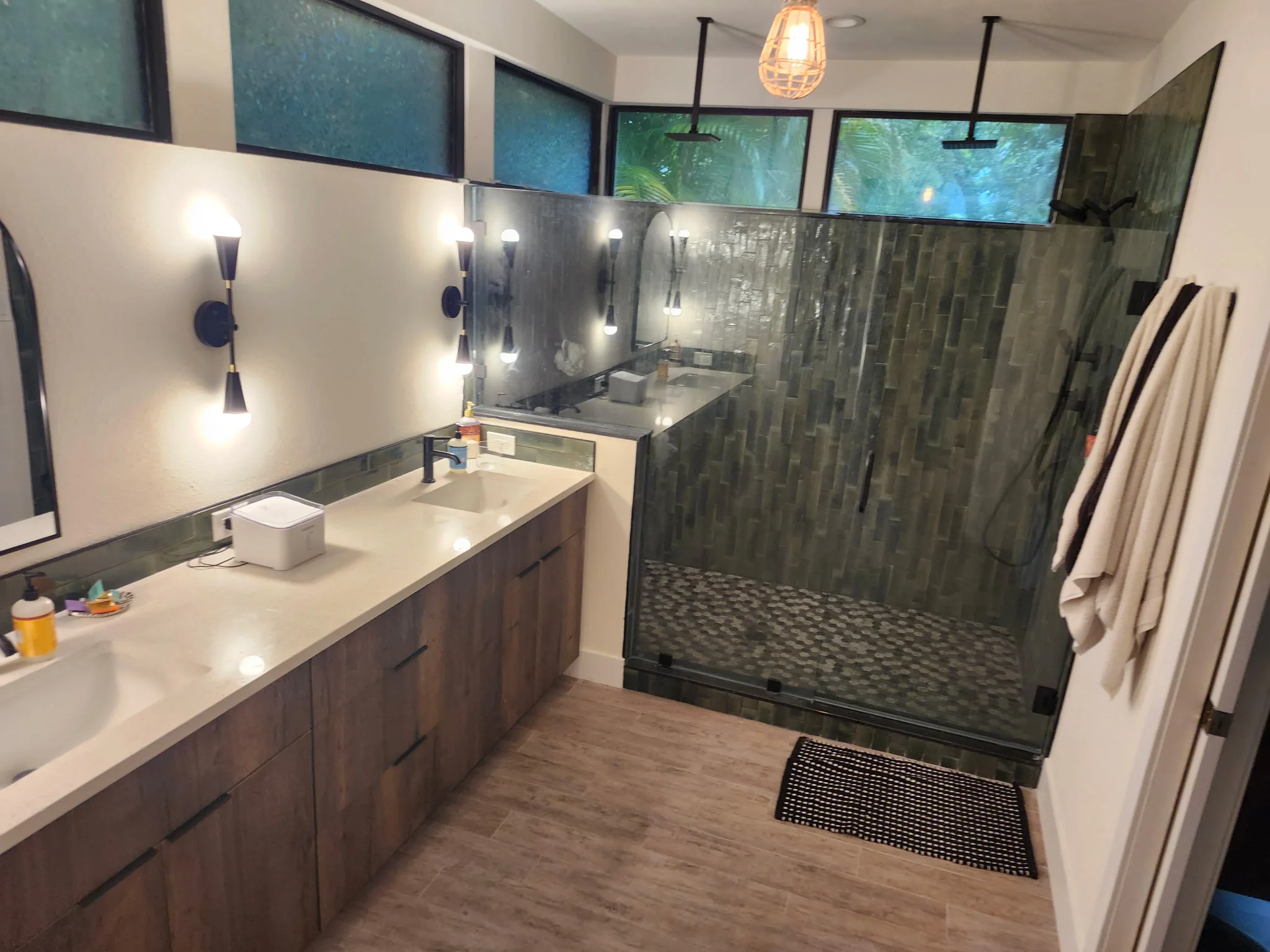 Bathroom with double vanity, white quartz counters, dark wood cabinets, and walk-in shower with green tile and glass enclosure