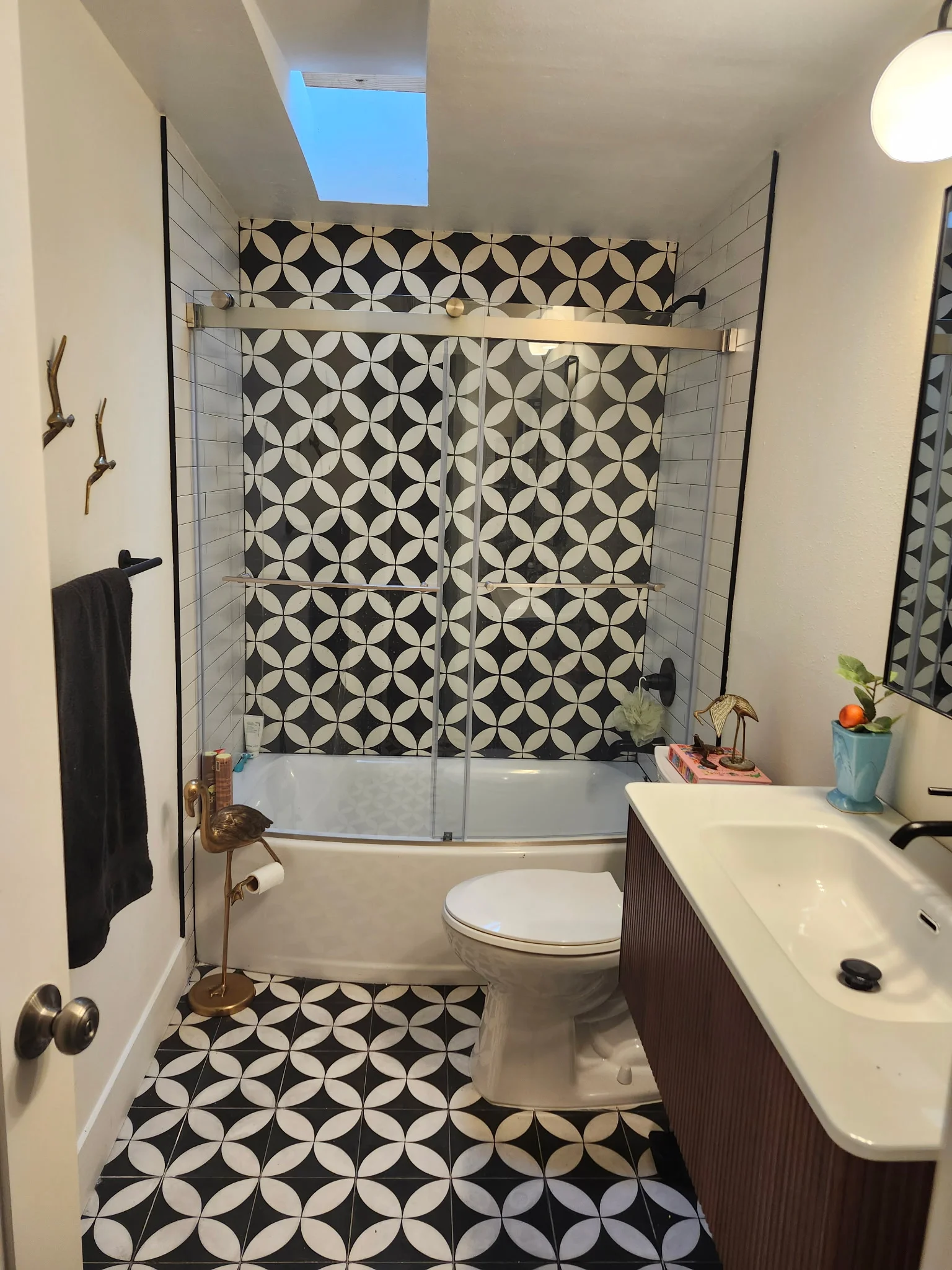Bathroom with black and white geometric tile shower surround and floor, frameless glass enclosure, white vanity