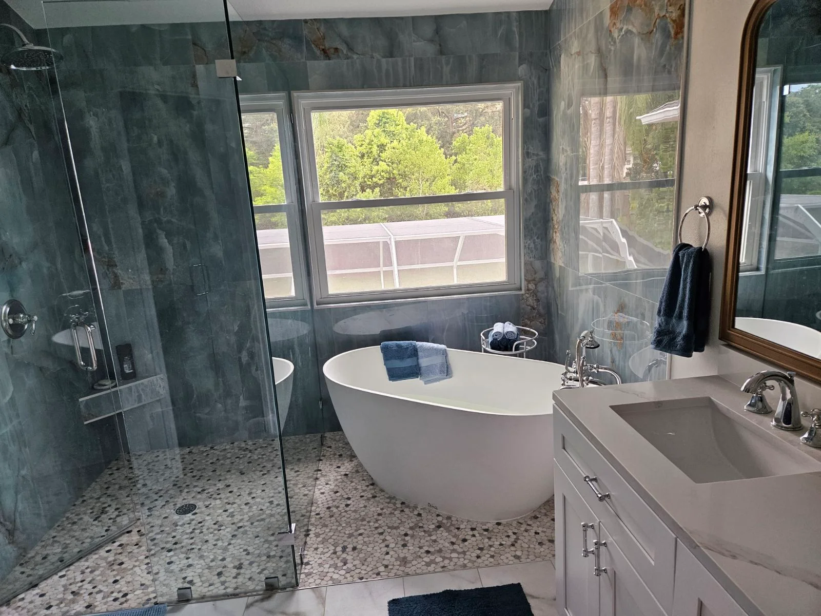 Modern bathroom with slate walls, freestanding tub, frameless shower, pebble floor, and white vanity