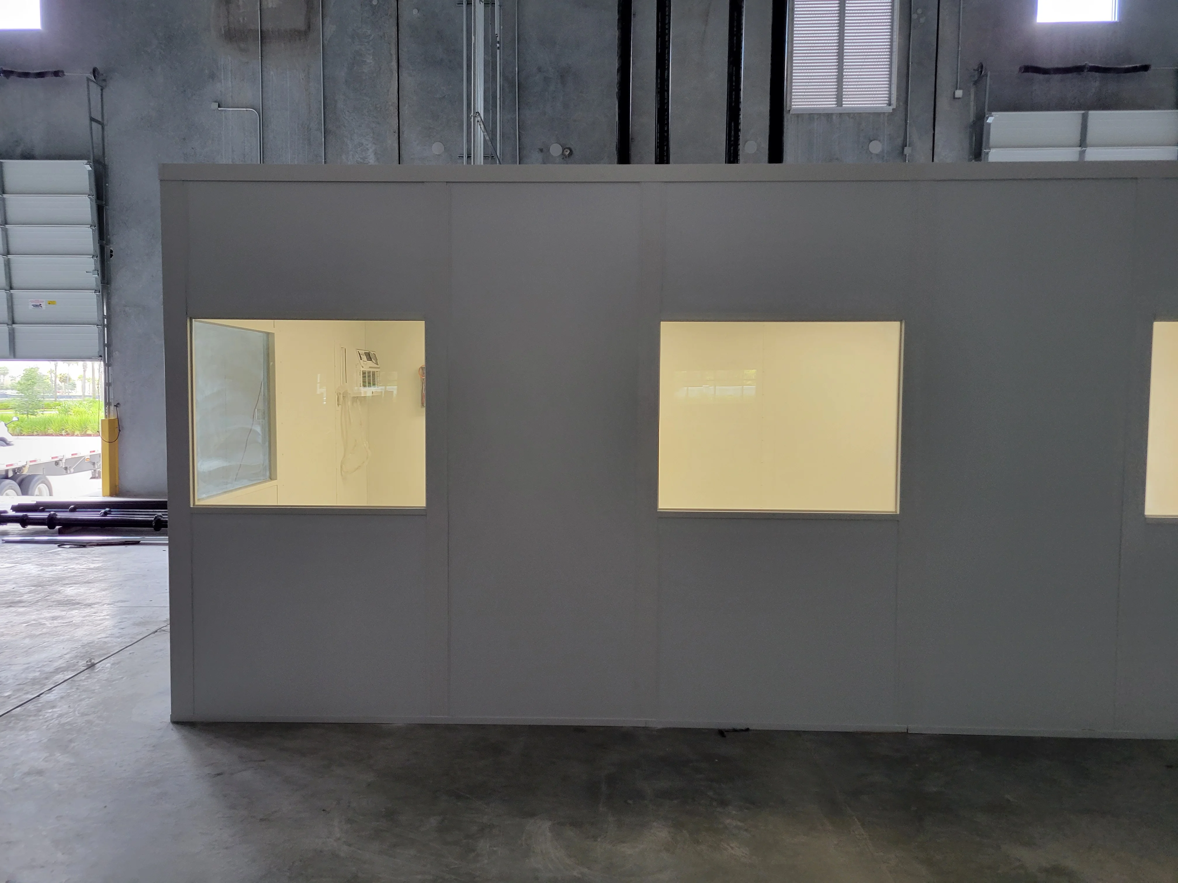 Gray drywall partition walls with brass-framed window openings and backlit yellow panels in commercial space