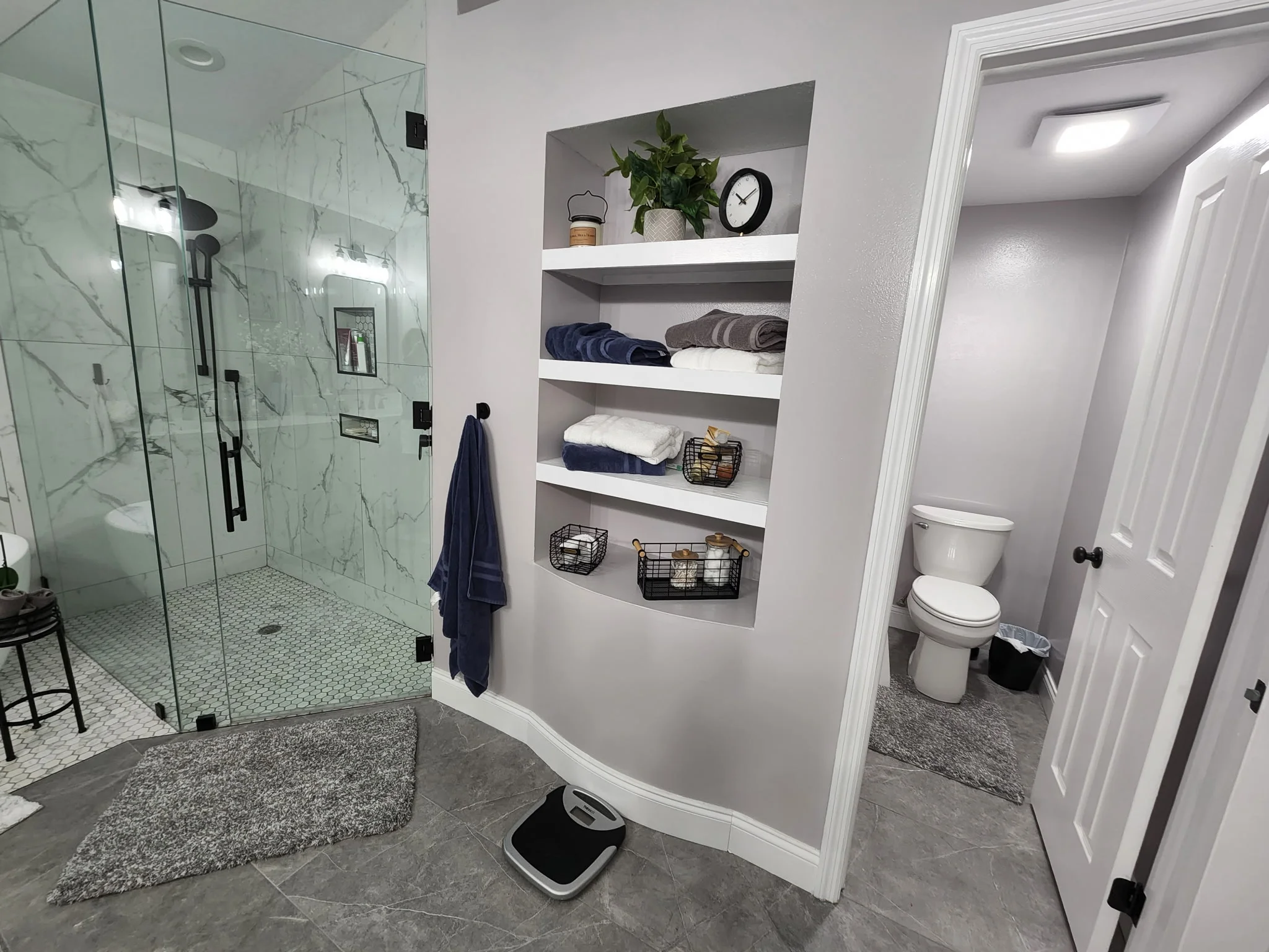 Bathroom with glass shower, marble tile, custom shelving, and porcelain flooring