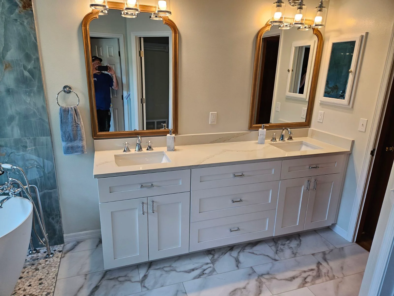 Dual-sink bathroom vanity with gray cabinetry, quartz countertop, marble flooring, and gold-framed mirrors