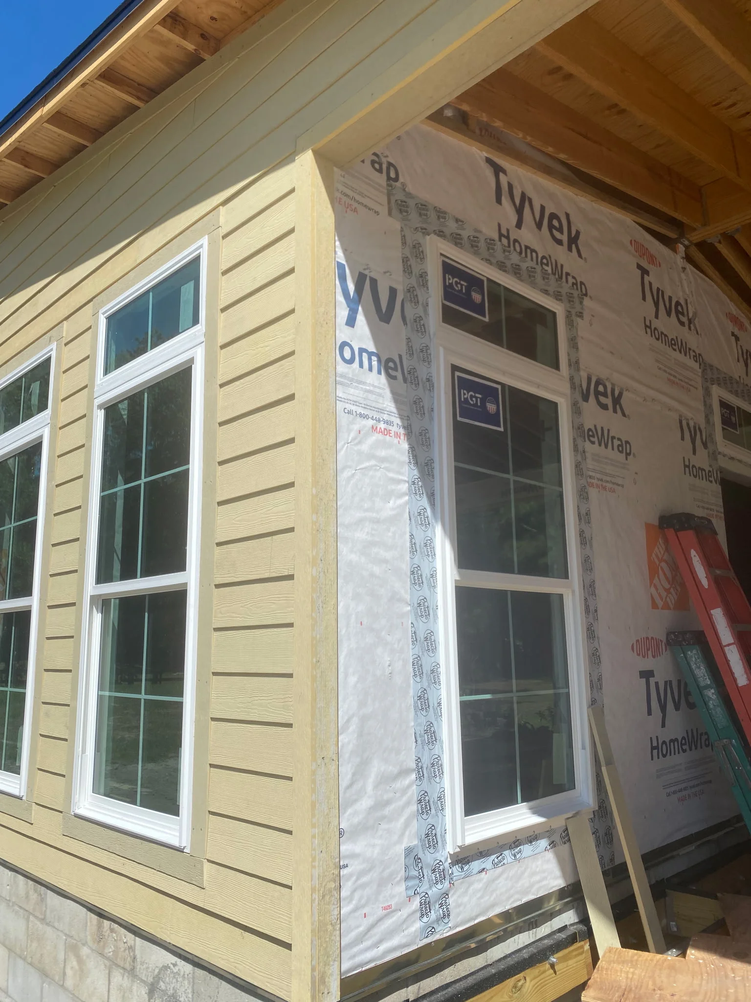 Yellow horizontal lap siding with white-trimmed windows and house wrap during new construction