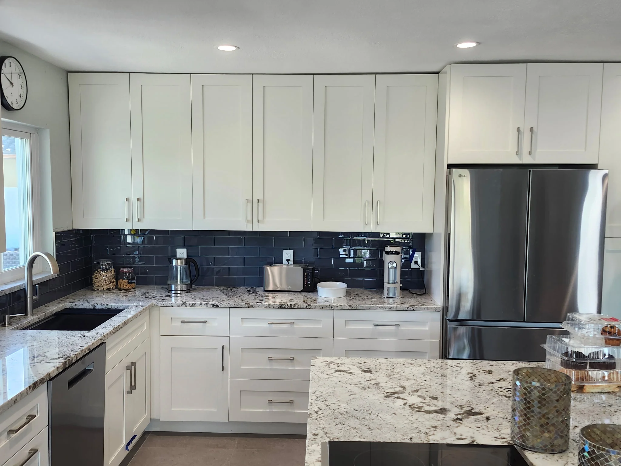 White cabinetry, granite counters, dark subway tile backsplash, stainless steel appliances