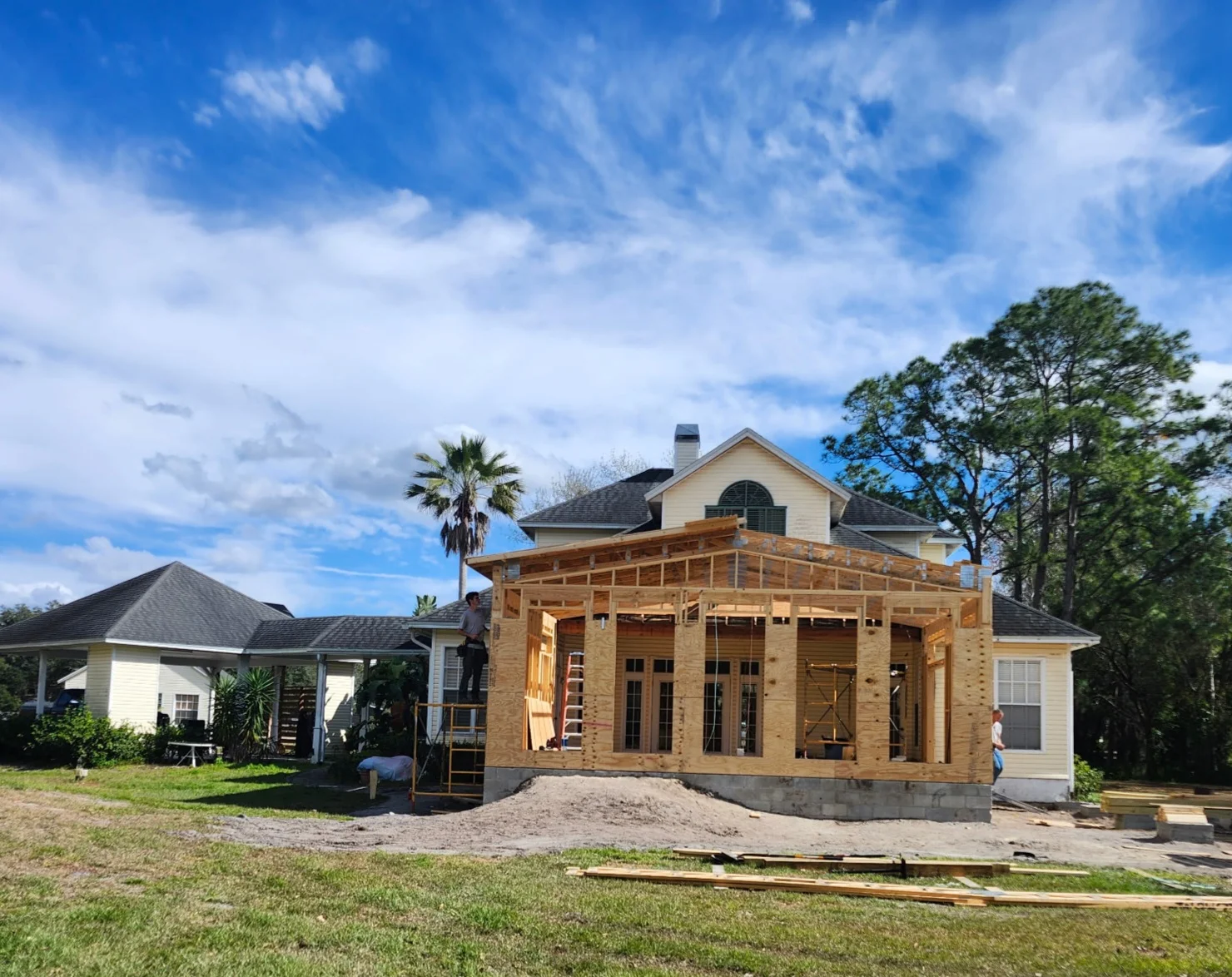 Wood-framed home addition with covered porch, concrete foundation, and French doors under construction