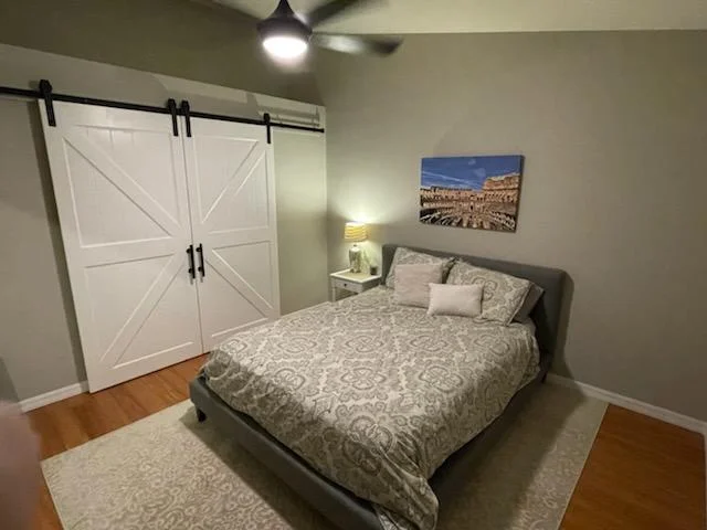 Master bedroom with hardwood floors, barn door closet, and ceiling fan