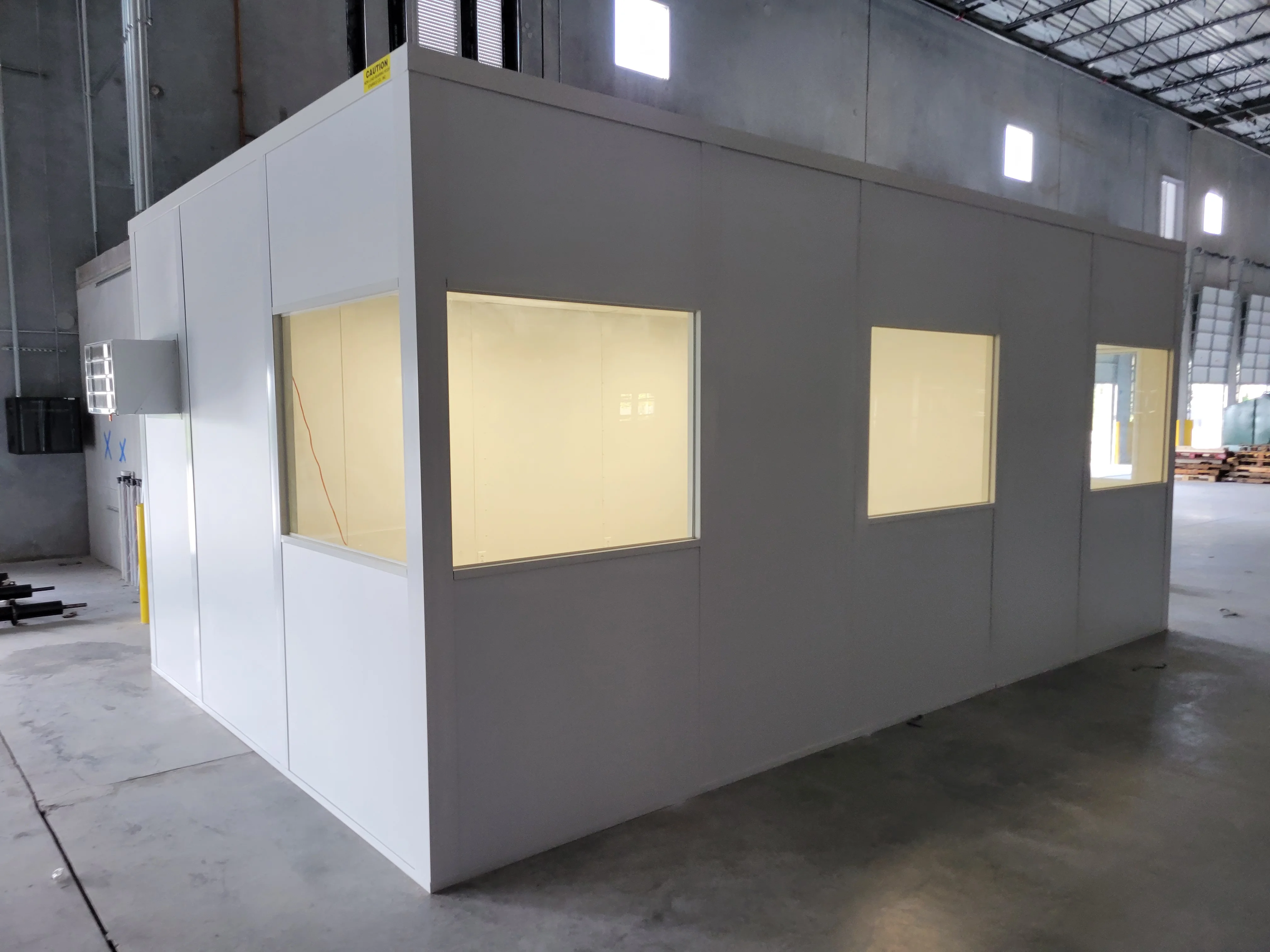 Drywall office enclosure with gray exterior, white panels, and illuminated window frames in warehouse